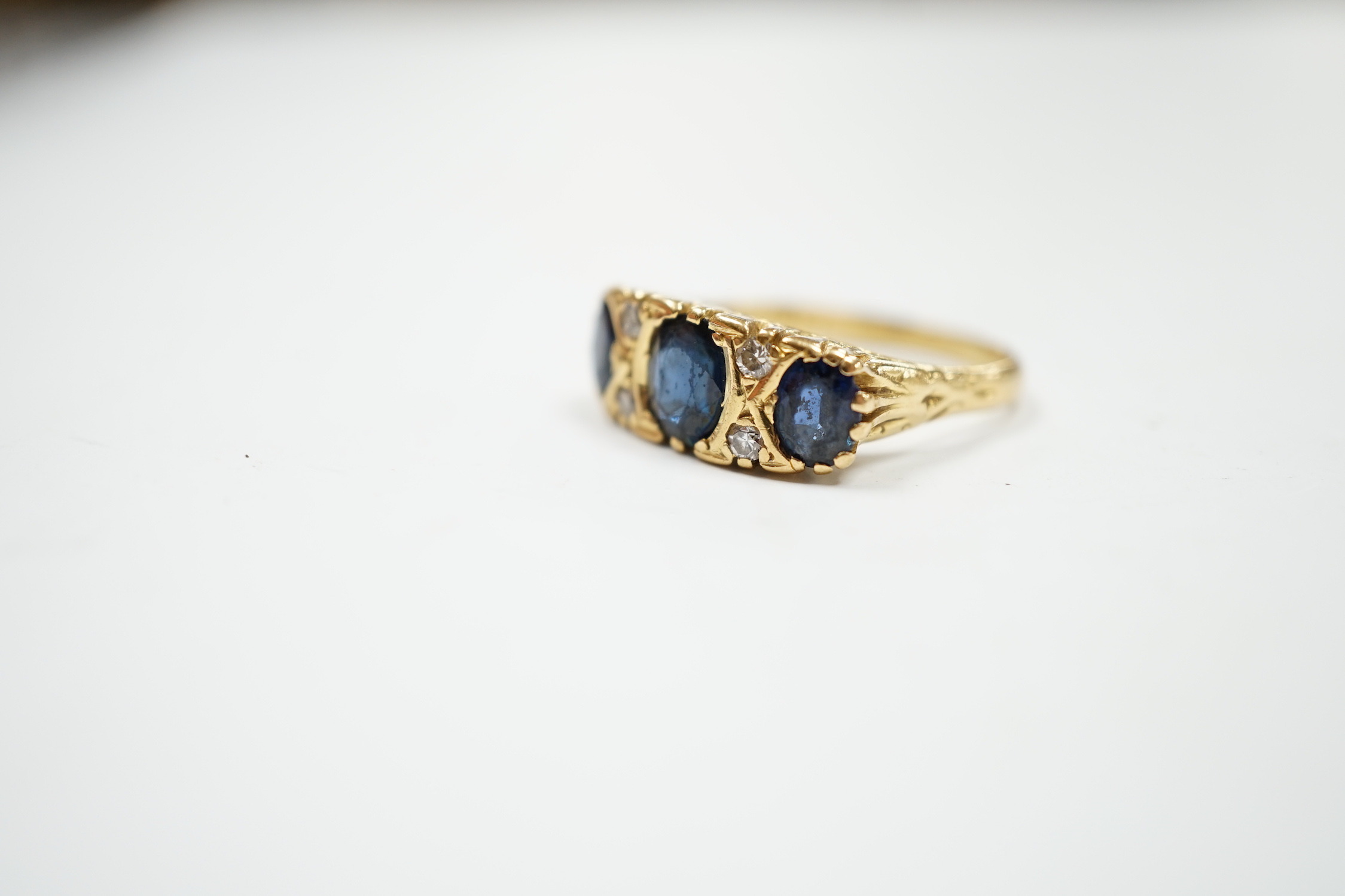 An 18ct and three stone sapphire set half hoop ring, with diamond chip spacers, size O, gross weight 6.2 grams.